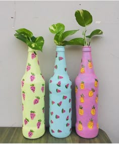 three painted vases with plants in them on a wooden table next to a wall