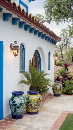 two large vases sitting on the side of a white building with blue trimming