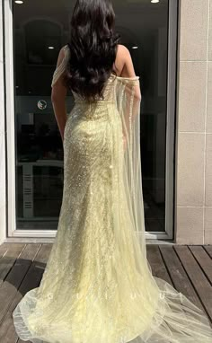 a woman in a yellow dress is standing on a wooden deck with her back to the camera