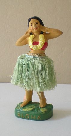 a figurine of a hula dancer on a green base with the word aloha written below it