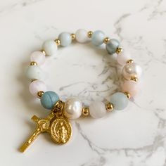 This decade rosary stretch bracelet is made with 8mm matte aquamarine and rose quartz gemstone beads, stretch cord, 10mm pearls, gold plated spacer beads and gold tone Italian made crucifix and Miraculous medal charms. The bracelet is 7 inches in length. Please send me an Etsy message if you need a different size. The bracelet will come packaged in a jewelry box to keep it safe on its journey to you. It's also perfect for gifting and would be a great addition to an Easter basket! Follow us on In Beads Packaging Ideas, Rosary Design, Blue Bracelets, Sacred Jewelry, Rosary Jewelry, Decade Rosary, Bracelets Design, Catholic Jewelry, Catholic Rosary