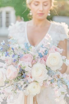 a woman holding a bouquet of white and pink flowers in front of her face while wearing a wedding dress