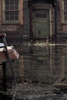 an old chair sitting in the middle of a flooded street next to a brick building