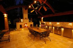 an outdoor kitchen and dining area lit up at night with lights on the patio ceiling