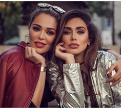 two women posing for the camera with their arms around each other and one is holding her hand on her chin