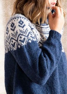 a woman wearing a blue and white sweater talking on a cell phone while standing in front of a wall