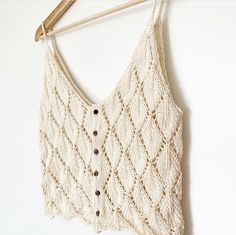 a white knitted vest hanging on a wooden hanger