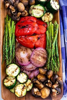 an assortment of vegetables are arranged in a wooden tray on a blue and white checkered tablecloth