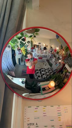 a young boy is taking a selfie in the reflection of a round mirror with plants on it