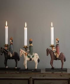 three small figurines are sitting on top of a table with candles in front of them