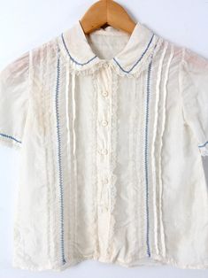 "This is a vintage silk blouse circa 1920s. The cream silk top features pin tuck pleats down the front with blue laced stitching and lace trim. It buttons closed. CONDITION In great condition. Approximate Fit: XS MEASUREMENTS Bust: 30\" ... 76.2 cm Length: 18\" ... 45.7 cm Shoulders: 12\" .. 30.5 cm Outside Sleeve: 8\" ... 20.3 cm HOW WE MEASURE * Blouse measured lying flat * Bust measured armpit to armpit * Length measured down the center of the back * Shoulders measured between the shoulder se Cheap Vintage Cream Tops, Silk Tops With Lace Trim For Daywear, Vintage Lace Collar Button-up Top, Vintage Blouse With Ruffled Collar And Button Closure, Vintage Lace Blouse With Ruffled Collar, Cream Blouse With Ruffled Collar For Daywear, Lace Blouse With Buttons For Daywear, Vintage Ruffled Blouse For Daywear, Vintage Ruffles Blouse For Daywear