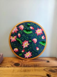 a painted plate sitting on top of a wooden table next to a pink flower pot