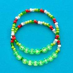 two bracelets with green and red beads on a blue surface, one has the word love spelled in white letters