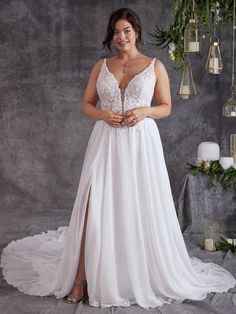 a woman in a white wedding dress standing next to a wall with candles and greenery