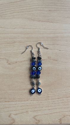 Crystal and bead earrings (obsidian & snowflake obsidian), with black evil eye in the center, and blue dangly evil eye at the base. Elegant Dangle Earrings With Evil Eye, Bohemian Blue Evil Eye Jewelry, Evil Eye Earrings Dangle, Cheap Blue Evil Eye Earrings, Evil Eye Crystal, Sterling Silver Evil Eye Dangle Earrings, Blue Evil Eye Dangle Earrings, Black Evil Eye, Obsidian Snowflake