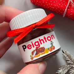 a hand holding a jar of peanut butter next to a christmas tree ornament