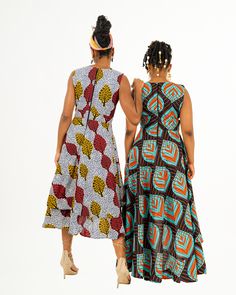 Two women posing in a red blue and black African print maxi dress and a yellow red and white African print maxi dress. Multicolor Print Sleeveless Midi Sundress, Sleeveless Multicolor Sundress Midi Dress, Fitted Sleeveless Maxi Dress With Layered Hem, Bohemian Sleeveless Multicolor Midi Dress, Bohemian Sleeveless Midi Dress In Multicolor Print, Multicolor Printed Dress With Asymmetrical Hem, Multicolor Asymmetrical Dress With Print, Multicolor Handkerchief Hem Dress, Multicolor Sleeveless Asymmetrical Dress