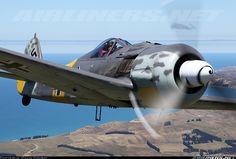 a fighter jet flying over the ocean with mountains in the background