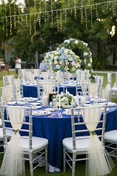 the tables are set with blue and white linens for an outdoor wedding reception at night