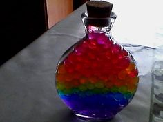 a glass bottle filled with lots of colorful liquid sitting on top of a table next to a window