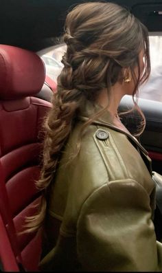 a woman sitting in the back seat of a car wearing a green jacket and braid