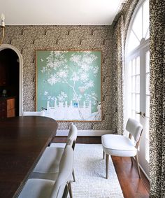 a dining room table and chairs in front of a wall with a painting on it