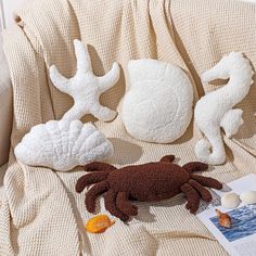 three stuffed animals sitting on top of a couch next to an open book and seashell