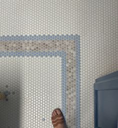 a person's feet standing in front of a bathroom wall with blue and white tiles