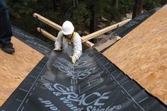 a man working on the roof of a house with wood shingles and tarps