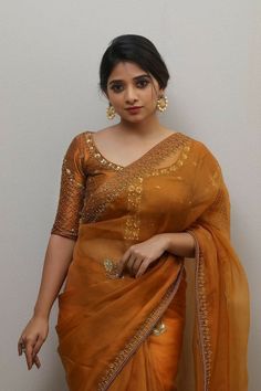 a woman in an orange sari posing for the camera with her hand on her hip