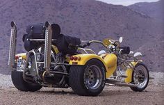 a yellow motorcycle with luggage strapped to it's back parked on the side of a dirt road