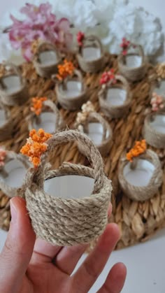 a hand holding a rope wrapped ring with orange flowers on it and candles in the background