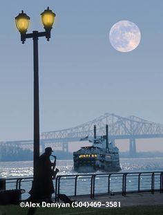 a man sitting on a bench next to a lamp post near the water with a boat in the background