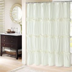 a white shower curtain with ruffles on it in front of a sink and mirror