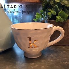 a white coffee cup sitting on top of a table next to a vase and potted plant