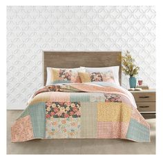 a bed covered in a colorful quilt next to a night stand with flowers on it