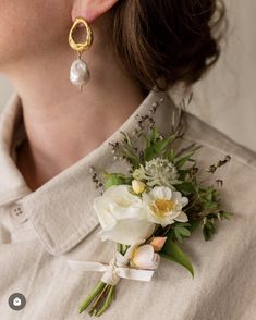 a close up of a person wearing earrings and a boutonniere with flowers