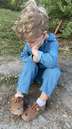 a little boy sitting on the ground with his hand under his chin