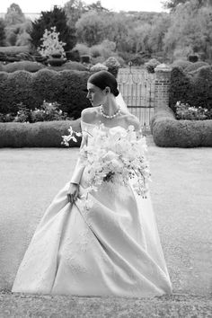 a woman in a wedding dress is walking down the street with flowers on her shoulder