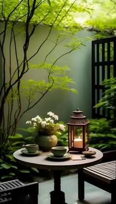 a small table with two tea cups and a lantern on it in front of some trees