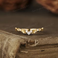 a gold ring with leaves and diamonds on top of a wooden table next to a book