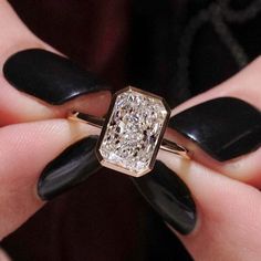 a woman's hand holding a ring with a diamond in it and black fingernails