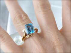 Dating to the 1970's, this vintage gold mounting features the sweeping lines and incredibly sleek styling of the mid-century style! We've set this gold ring with a pretty, perfectly faceted blue topaz of a lovely Caribbean hue! Metal: 14K Yellow Gold Gem: Blue Topaz 4.38 Carats Gem Measurements: 10.1 x 8.1 mm, Rectangle Emerald Cut Ring Size: 6.50 Marks: "14KPALL>>A" Stamped on the inside band Topaz Cocktail Ring, Emerald Cut Ring, Emerald Cut Rings, Mid Century Style, Cocktail Ring, Eternity Bands, Cocktail Rings, Emerald Cut, Vintage Gold