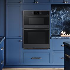 two black ovens in a blue kitchen with marble counter tops