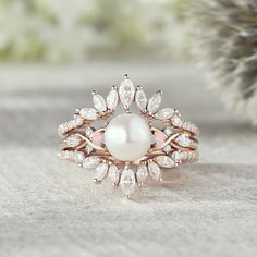 a pearl and diamond ring sits on a table next to a pine cone with leaves