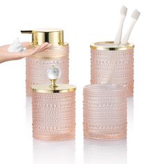 two pink glass containers with toothbrushes in them and one holding a gold cup