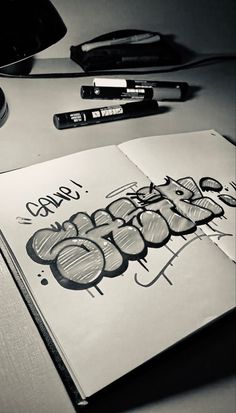 an open notebook with graffiti on it next to some pens and a computer mouse in black and white