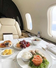 an airplane meal is on the table in front of two windows, with fruit and bread