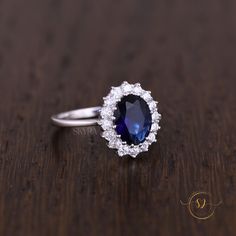 an oval shaped blue and white diamond ring on a wooden surface with the center stone surrounded by smaller round diamonds