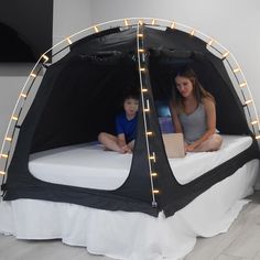 a woman and child are sitting in a tent bed with lights on the side of it